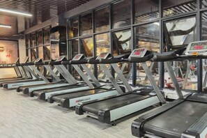 A row of treadmills in a gym with large windows and a modern ceiling design. - Huangting Hotel (Xintian)