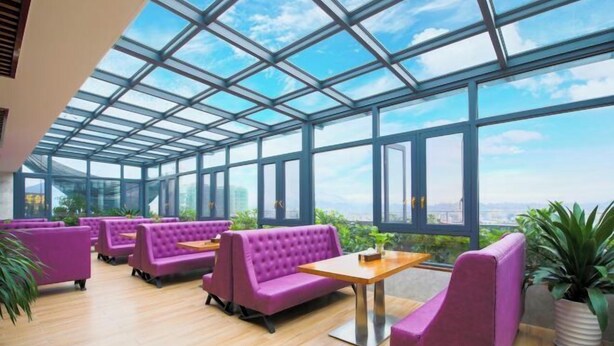 A modern indoor space with large windows and a glass ceiling, featuring purple seating and a wooden table.