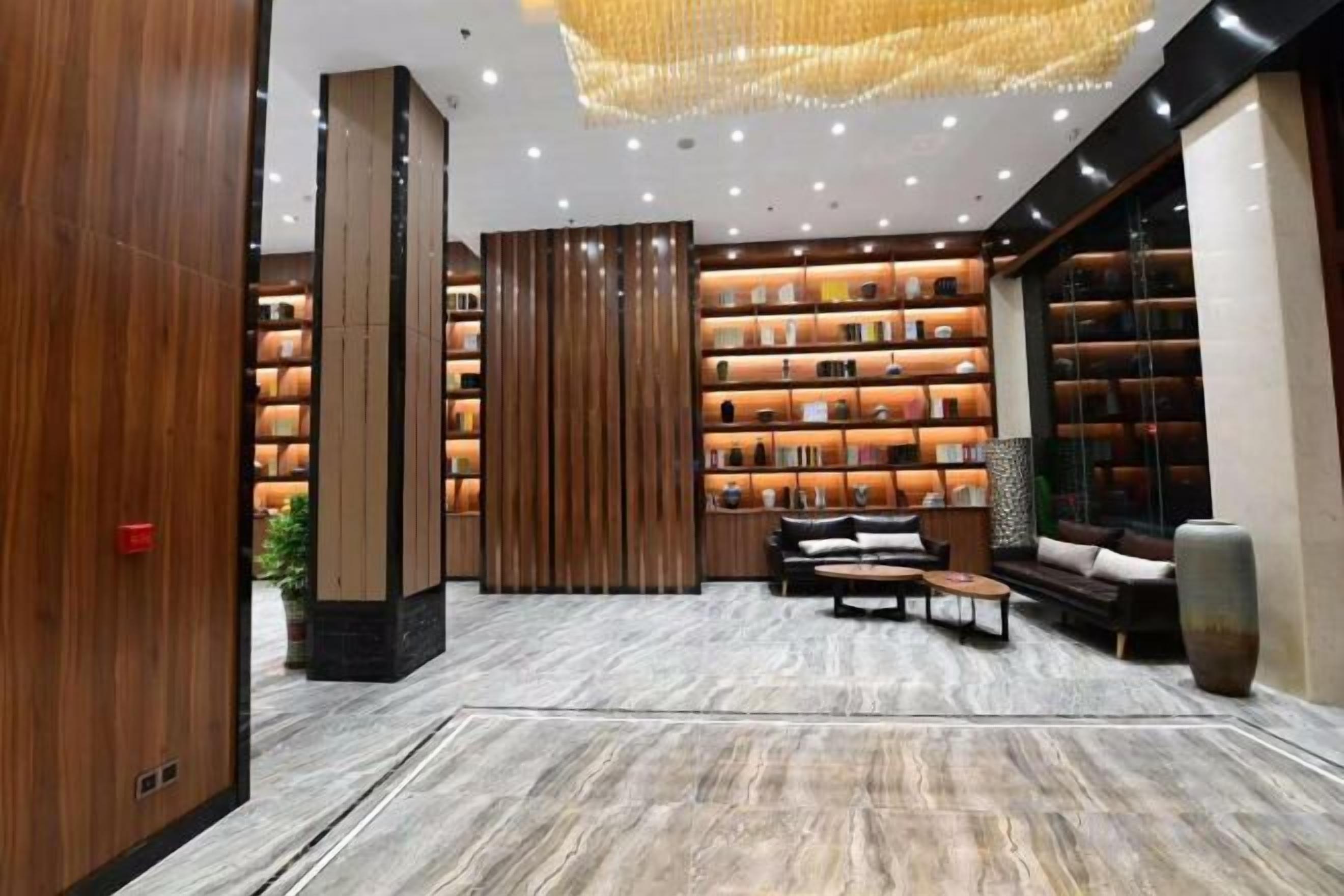 A modern lobby with a marble floor, wooden paneling, and a large chandelier.