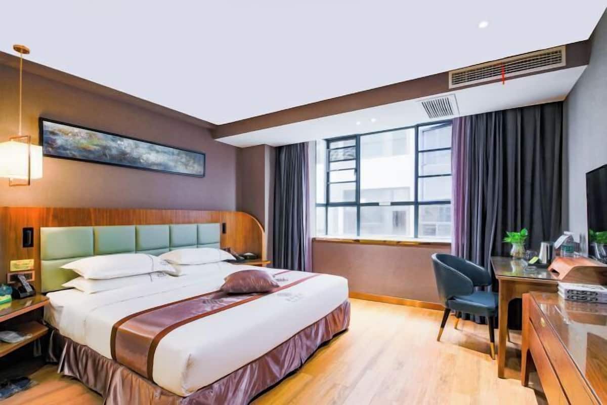 A hotel room with a bed, bedside table, desk, chair, and a large window.