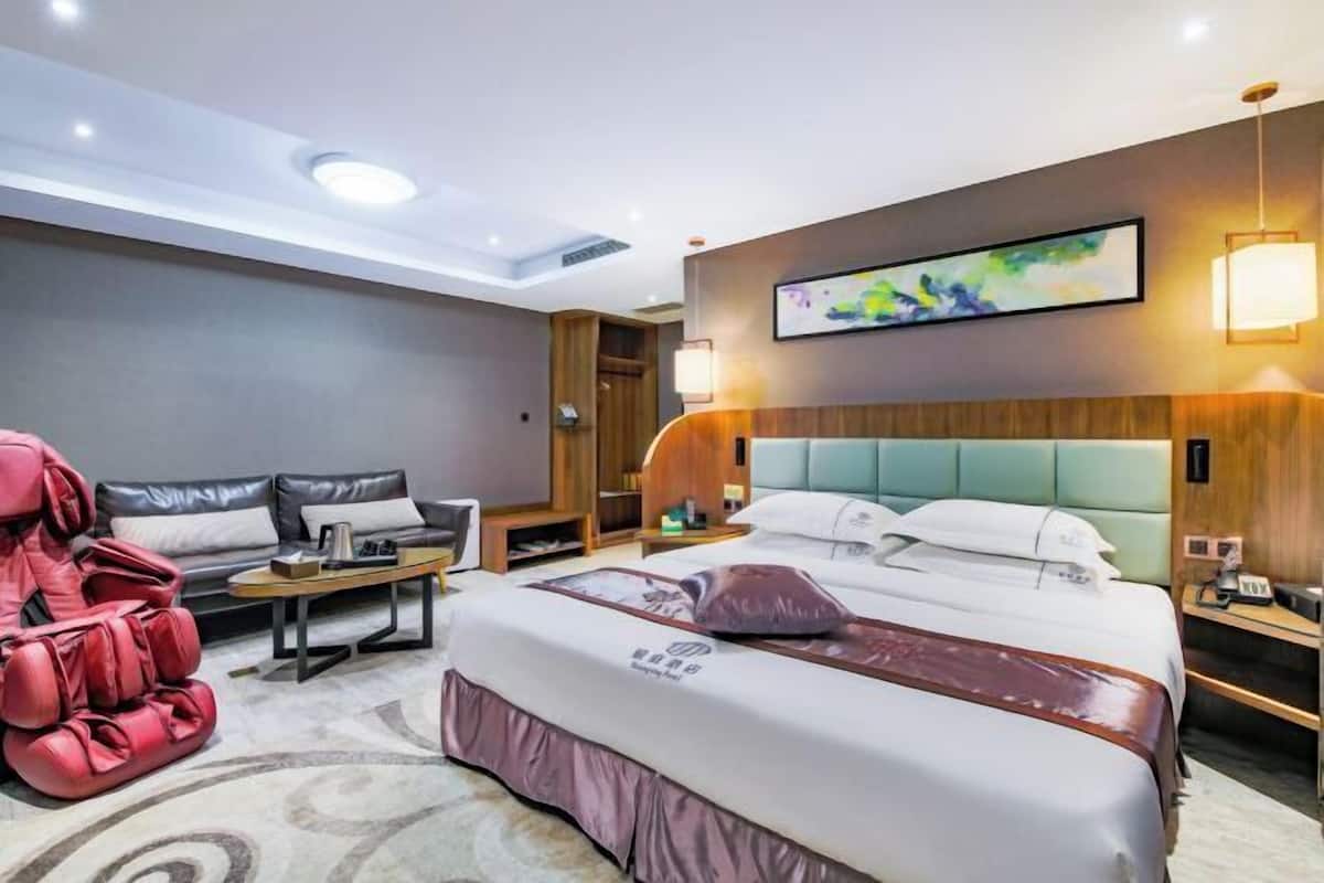 A hotel room with a large bed, a massage chair, a sofa, a desk, and a wall-mounted artwork.