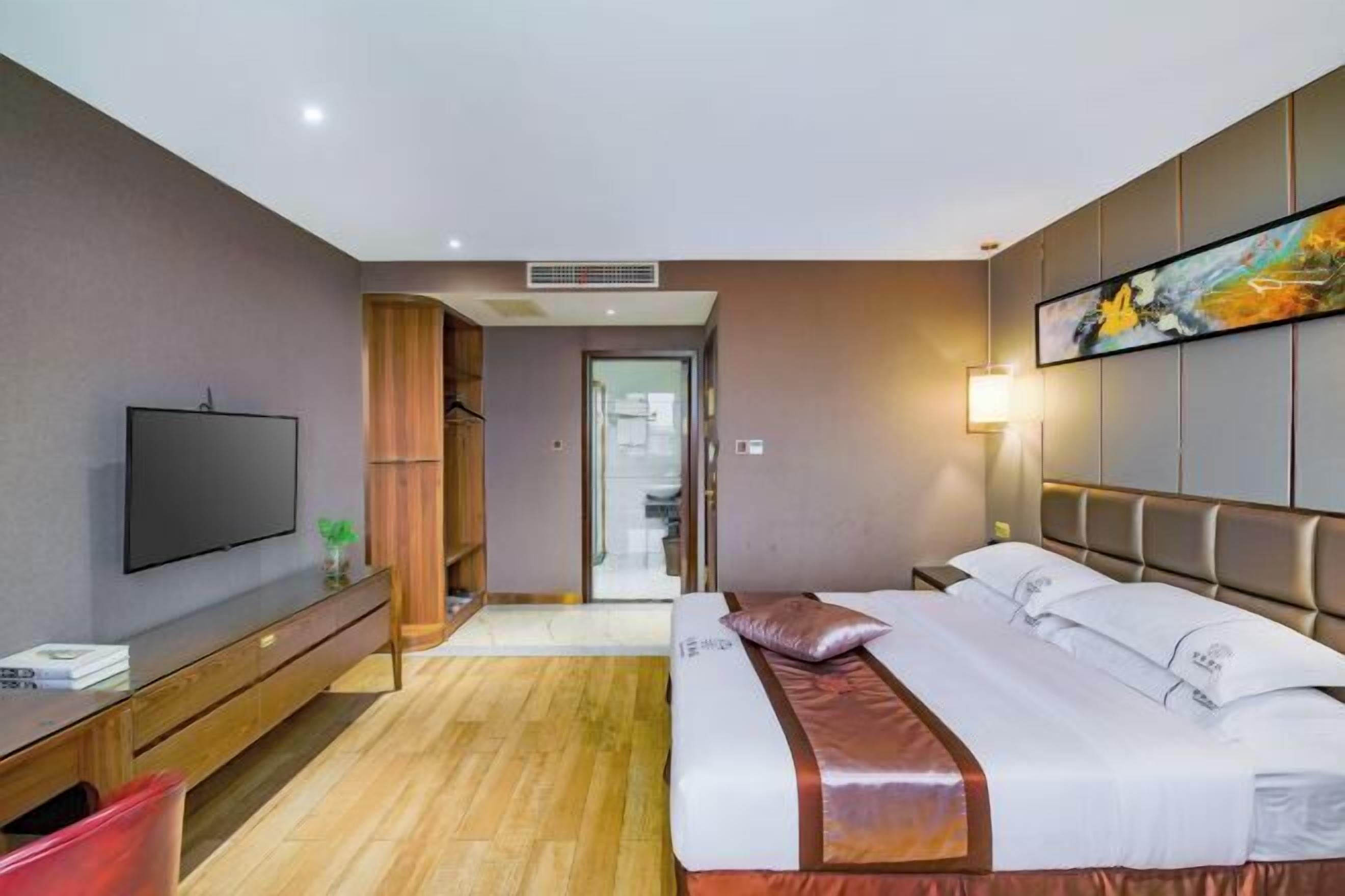 Een hotelkamer met een bed, een televisie, een bureau en een schilderij aan de muur.