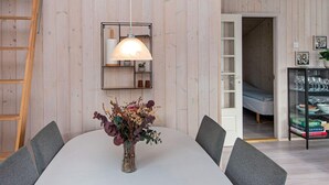 Un coin repas comprenant une table, des chaises, un vase avec des fleurs, une lampe suspendue et une échelle appuyée contre le mur.