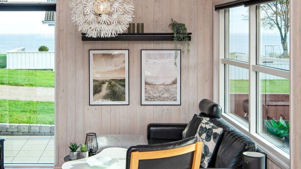Un salon moderne avec une grande fenêtre, un canapé en cuir noir, une chaise en bois, une table blanche et deux tableaux encadrés accrochés au mur.