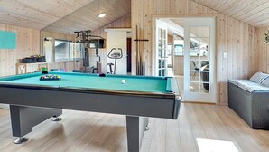 Une table de billard dans une pièce aux murs et au plafond en bois, avec un canapé et du matériel d’exercice.