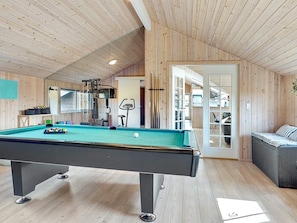 A pool table in a room with wooden walls and a ceiling, a sofa, and exercise equipment.