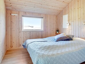 A bedroom with a wooden ceiling, a window, a bed with a quilt, and a bedside table with a plant. - 10 Person Holiday Home in Lokken (Lokken)