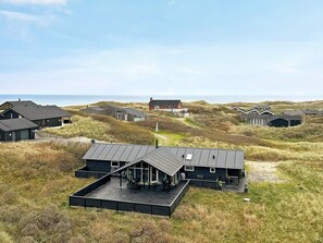 Een landgoed aan de kust met meerdere gebouwen, waaronder een opvallend huis met een groot terras en een kleinere constructie in de buurt.