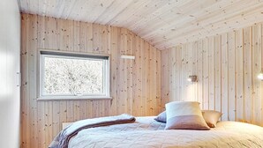 Une chambre avec un mur lambrissé en bois, une fenêtre donnant sur un beau paysage, un lit avec des oreillers et une lampe de chevet.