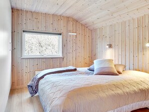 A bedroom with a wooden paneled wall, a window with a view, a bed with pillows, and a bedside lamp.