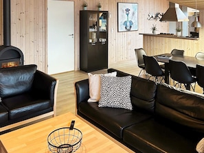 A modern living room with a fireplace, leather sofas, a dining area with a table and chairs, and a kitchen visible in the background. - 10 Person Holiday Home in Lokken (Lokken)