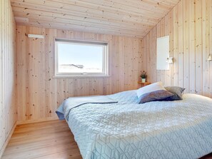 A bedroom with a wooden ceiling, a window with a view, a bed with a quilt, and a nightstand with a plant. - 10 Person Holiday Home in Lokken (Lokken)