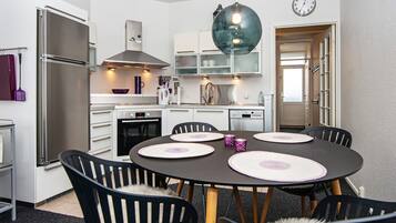 A modern kitchen with white cabinets, a stainless steel refrigerator, a built-in oven, and a dining area with a round table and chairs.