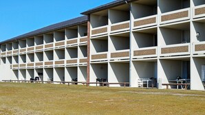 A multi-story building with a grid of rooms, outdoor seating, and a clear sky.