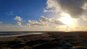 A beach with a clear sky, a visible moon, and a sunset.