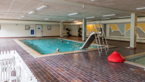 An indoor swimming pool with a slide, tiled flooring, and a ceiling with fluorescent lights.