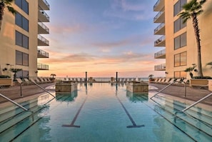 A swimming pool with a sunset view, surrounded by buildings with balconies.
