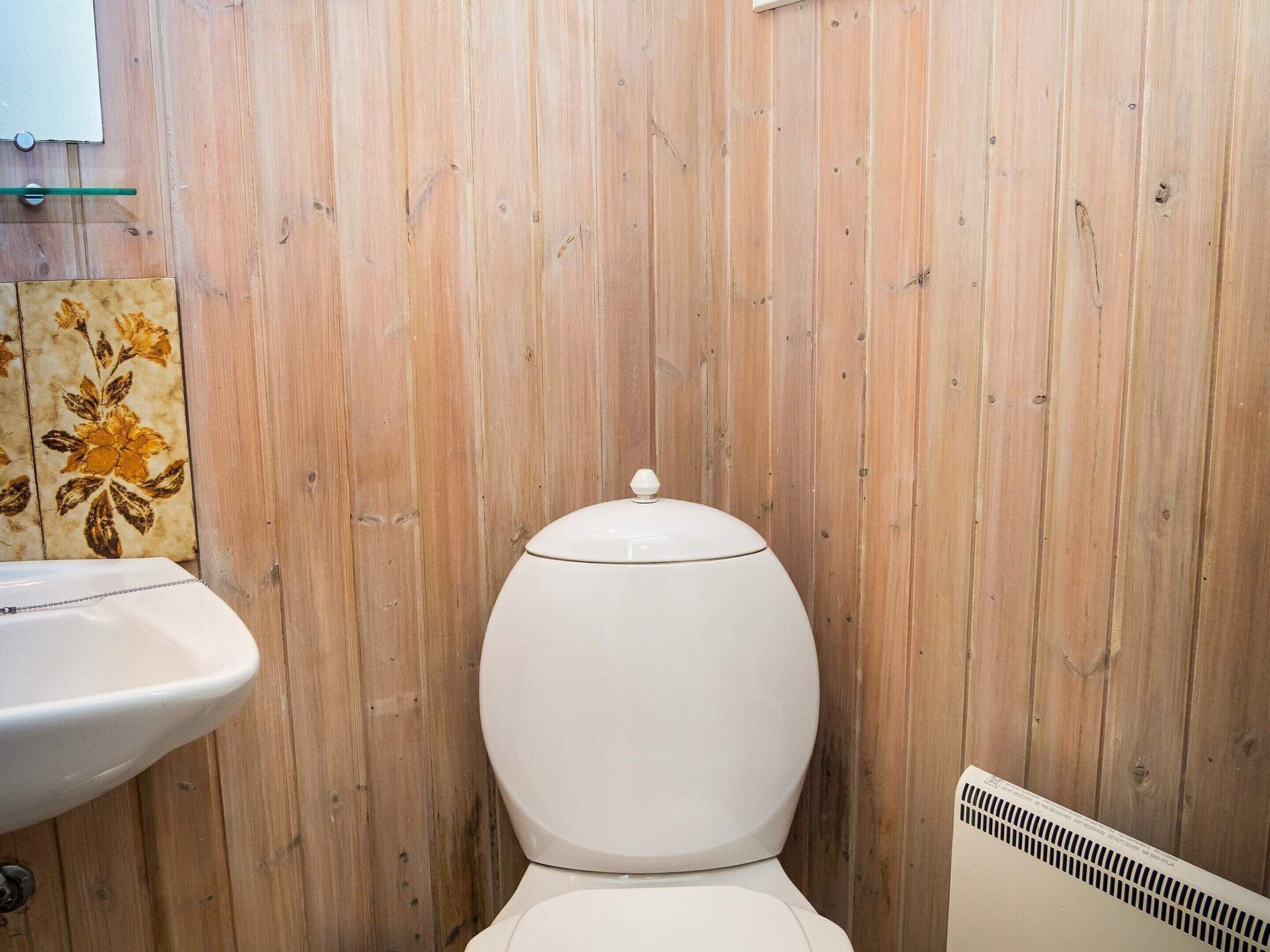 Ein Badezimmer mit Holzwand, Toilette und Waschbecken – alles in Weiß.