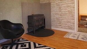 Habitació amb una cadira de cuir negre, un petit escalfador negre, una catifa amb dibuixos i una paret amb aspecte de pedra.