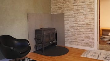 Una habitación con una butaca de cuero negro, una estufa pequeña negra, un tapete estampado y piso de madera.