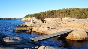 A rocky shoreline with a wooden dock extending into calm water, surrounded by dense forest. - 4 Person Holiday Home in Lur (Lur)