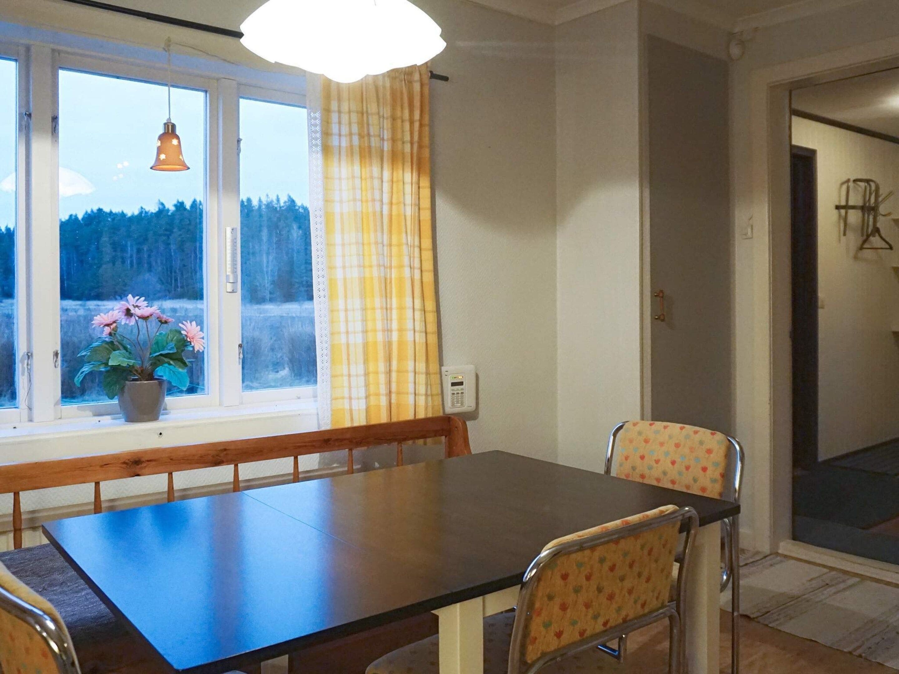 Un comedor con una mesa y sillas, una ventana con vistas a árboles, y una lámpara colgante.