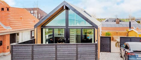 A modern house with a sloped roof, large windows, and a wooden fence.