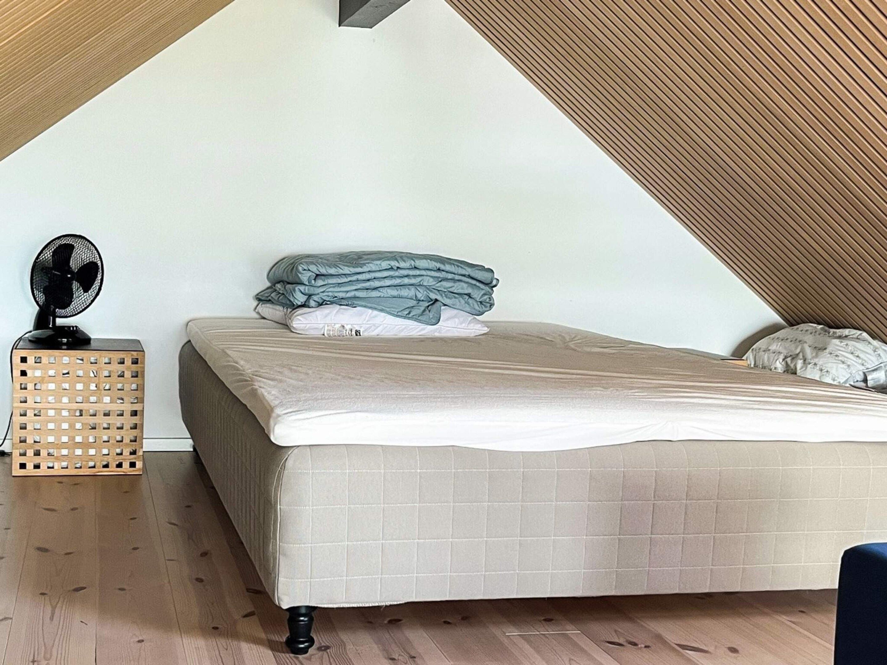 A bedroom with a bed, a fan, and a wooden crate.