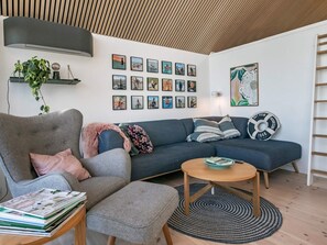 A modern living room with a grey sofa, a round wooden coffee table, and a bookshelf with magazines. - 6 Person Holiday Home in Otterup (Otterup)
