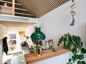Un intérieur moderne avec un plafond en bois, une lampe verte, une étagère ornée d’une plante et un panneau indiquant « Confiseries et chocolats ».