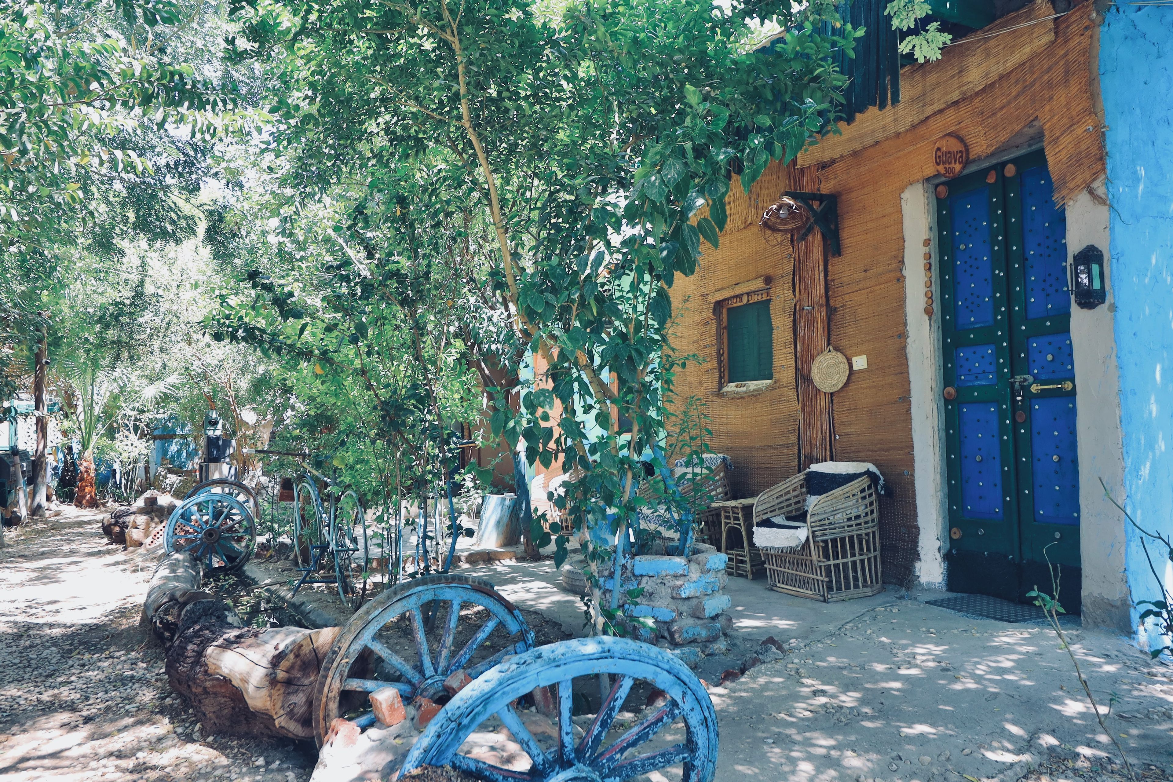 A rustic outdoor setting with a traditional building, a blue door, and vintage farming equipment.