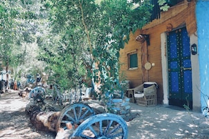 A rustic outdoor setting with a traditional building, a blue door, and vintage farming equipment.