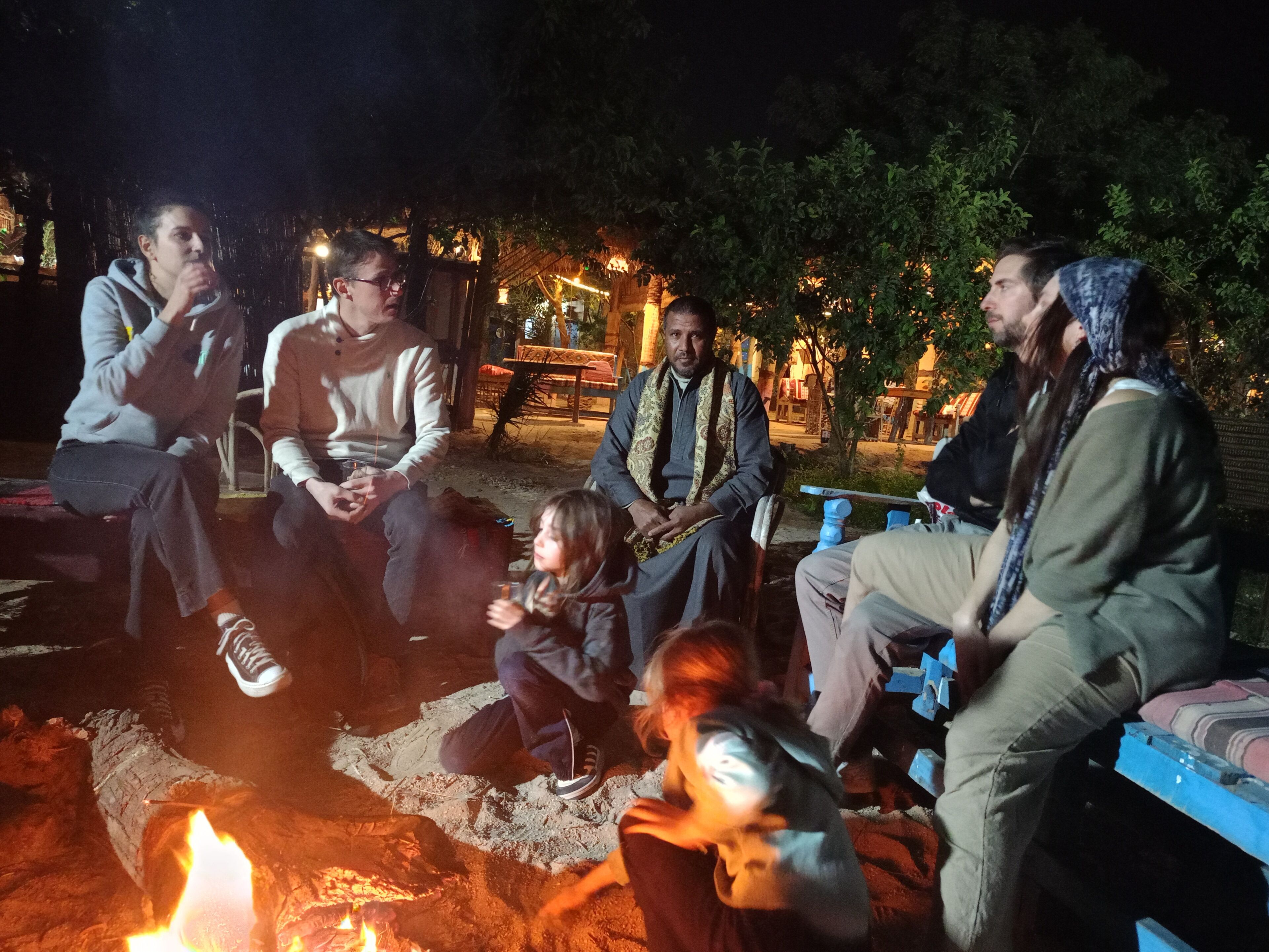 A group of people sitting around a campfire at night.