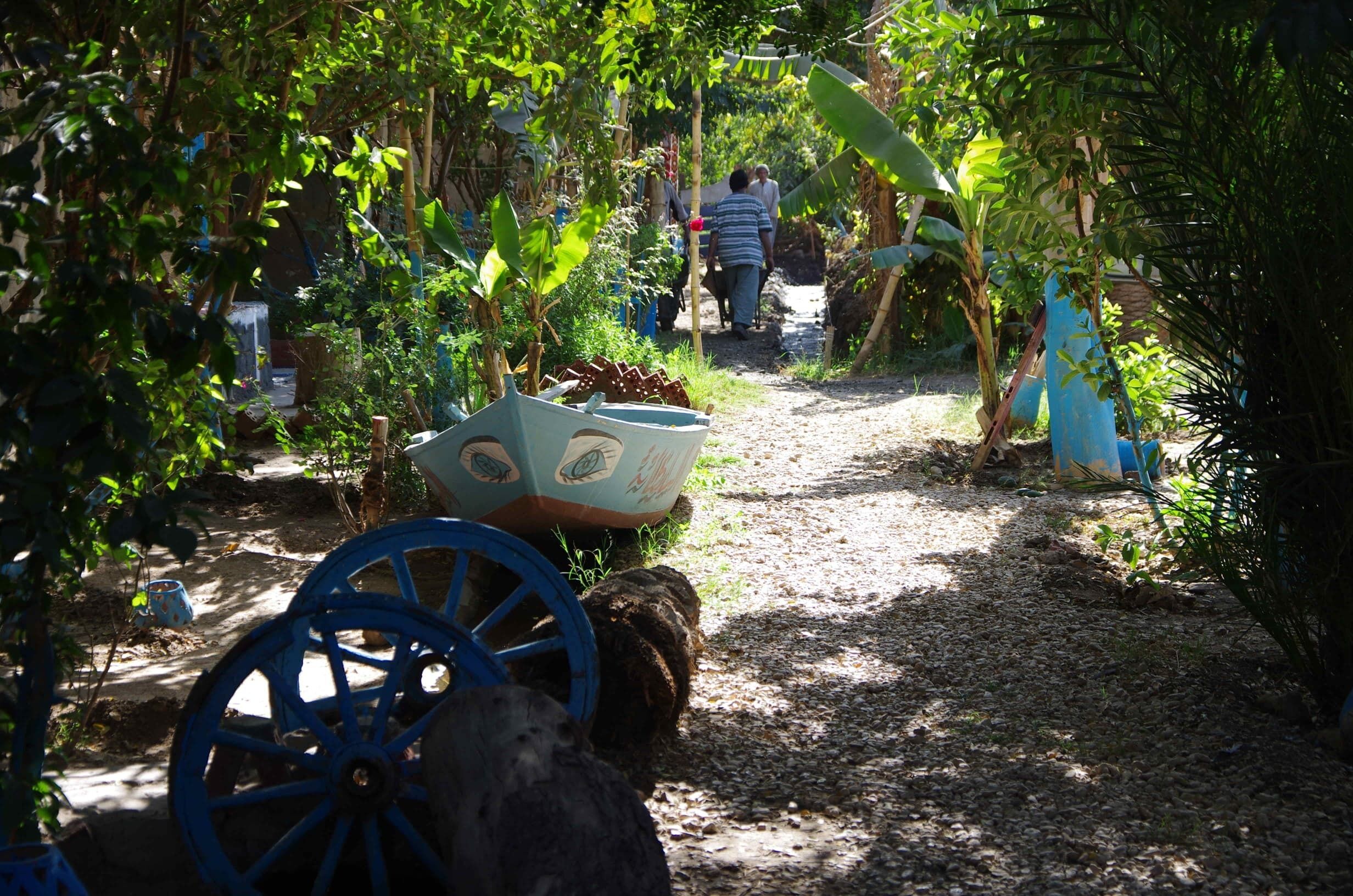 A garden path with a wheelbarrow, a blue cart, and a person walking away.