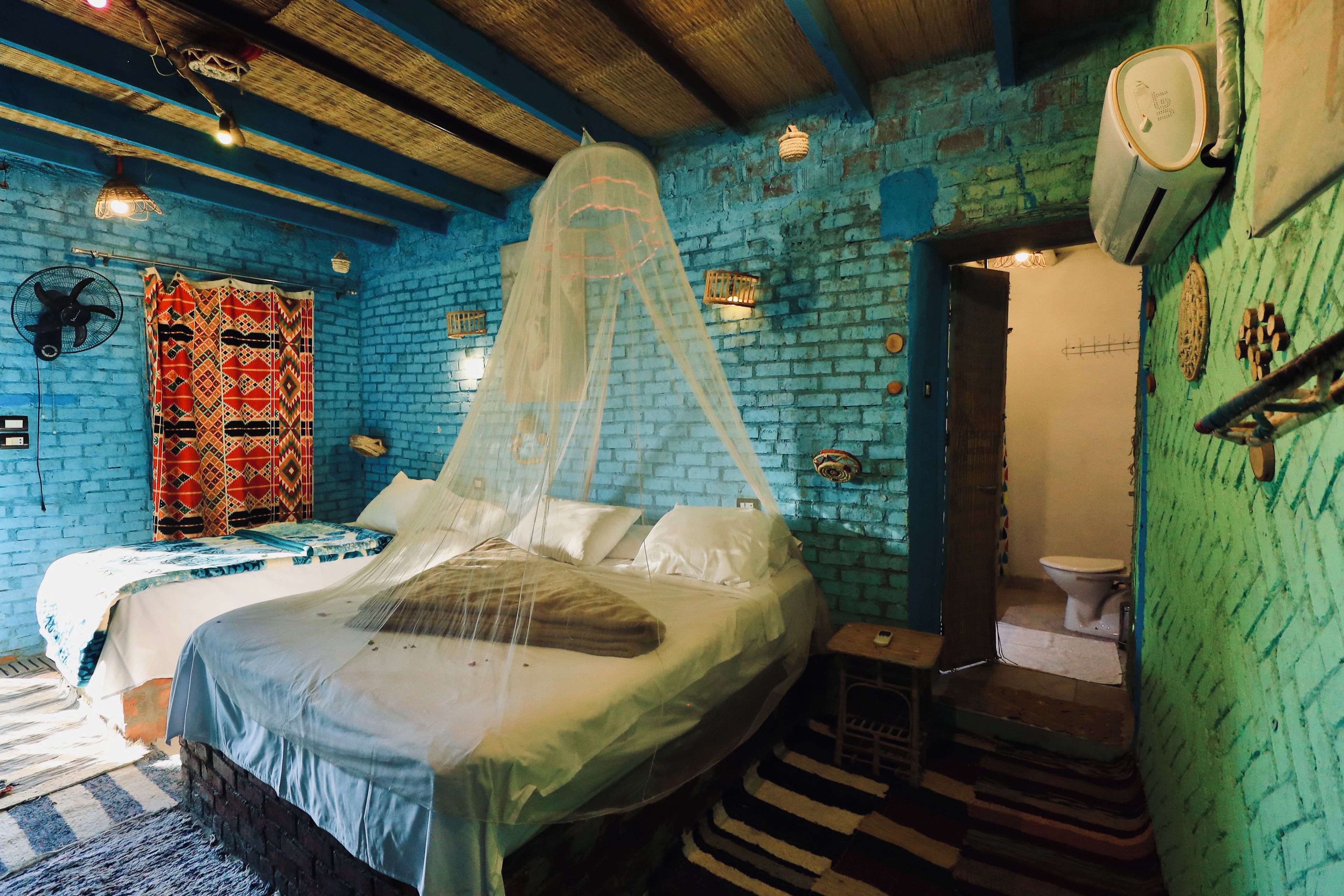 Una habitación con cama, ventilador, mosquitero y baño con inodoro.