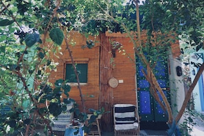 Una estructura rústica de madera con un ventanal verde, una puerta tejida y una puerta azul.