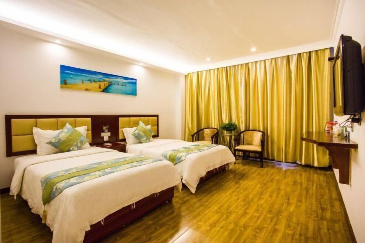 Habitación de hotel con dos camas, piso de madera, un cuadro en la pared, una silla y un escritorio con una lámpara.