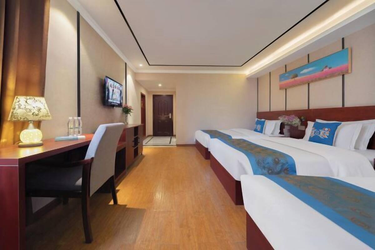 Una habitación de hotel con escritorio, dos camas, televisor y un cuadro en la pared.