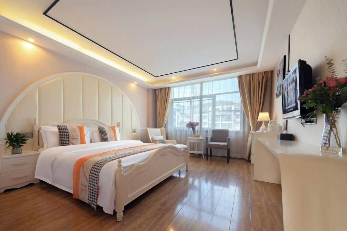 Una habitación de hotel con cama, mesitas de noche, un escritorio y una ventana con cortinas.