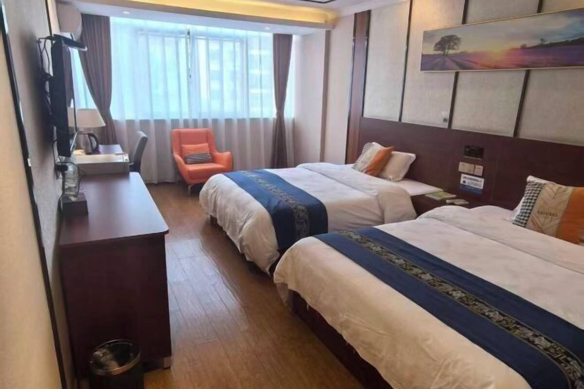 Habitación de hotel con dos camas, un escritorio, una silla y una ventana con cortinas.