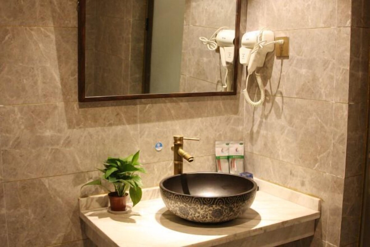 A bathroom with a marble sink, a potted plant, a hairdryer, and a mirror.
