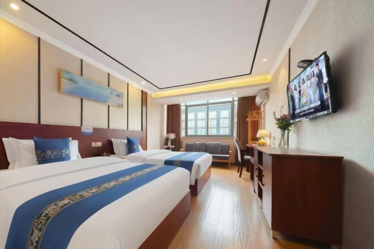 Habitación de hotel con dos camas, un escritorio, un televisor y una ventana.