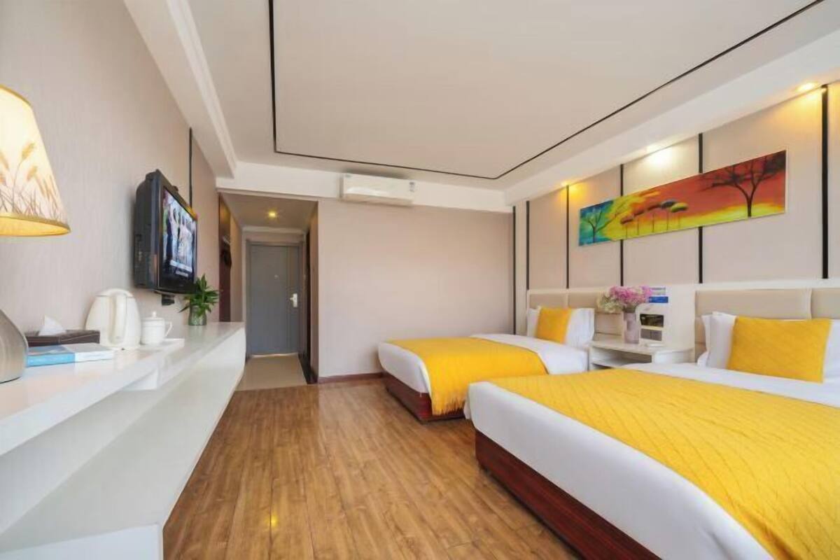 Habitación de hotel con dos camas, televisión, escritorio con lámpara y un cuadro en la pared.