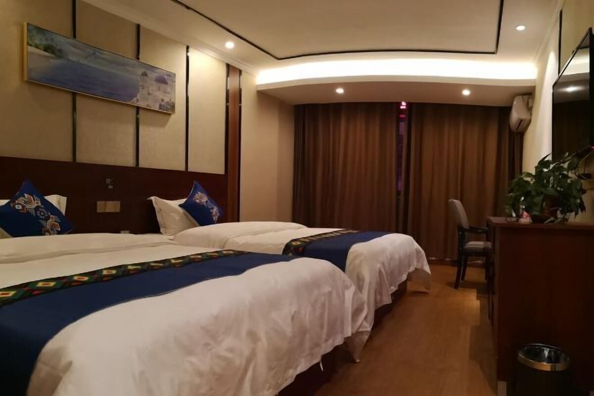 A hotel room with two beds, a painting on the wall, a curtain, a chair, and a trash bin.