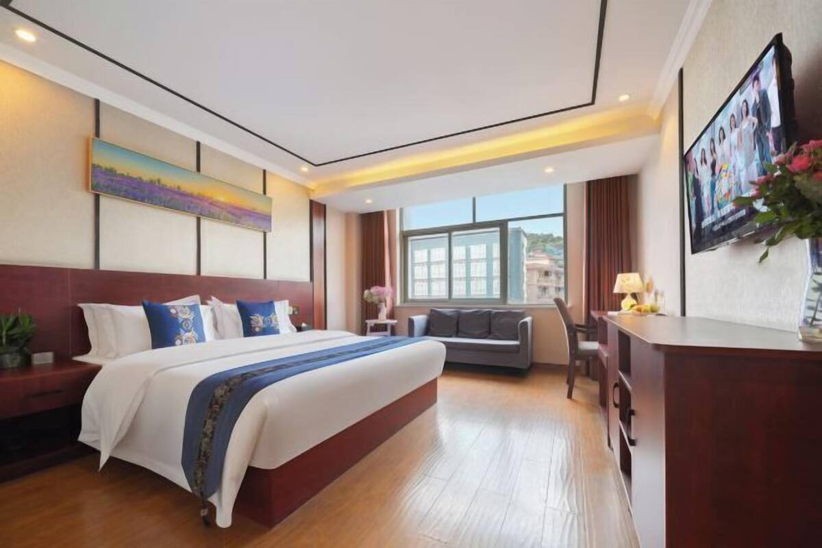 Una habitación de hotel con una cama grande, un escritorio, un sofá, un televisor y una ventana.