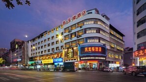 A multi-story hotel with illuminated signage, a curved facade, and a street view with cars and other buildings. - Dongyulou Hotel (Jishou University Zhangjiajie Campus) (Zhangjiajie)