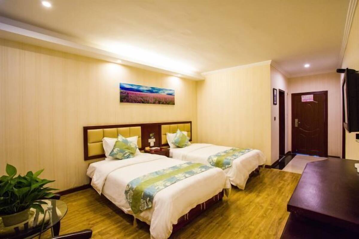 Habitación de hotel con dos camas, piso de madera, un cuadro en la pared y un televisor montado.