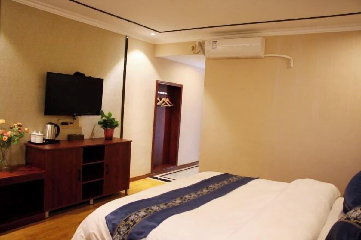 A hotel room with a bed, a TV mounted on the wall, a wooden dresser, and a potted plant.