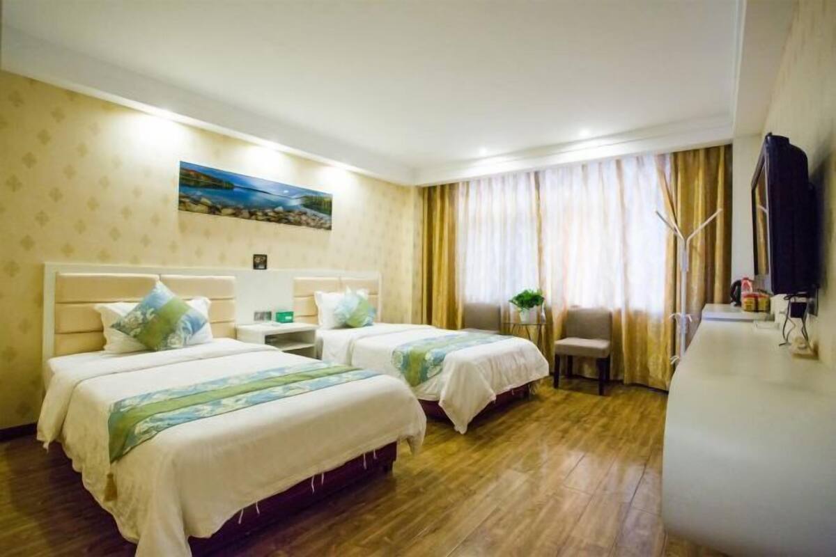 Habitación de hotel con dos camas, un escritorio, una silla, un televisor y un cuadro en la pared.