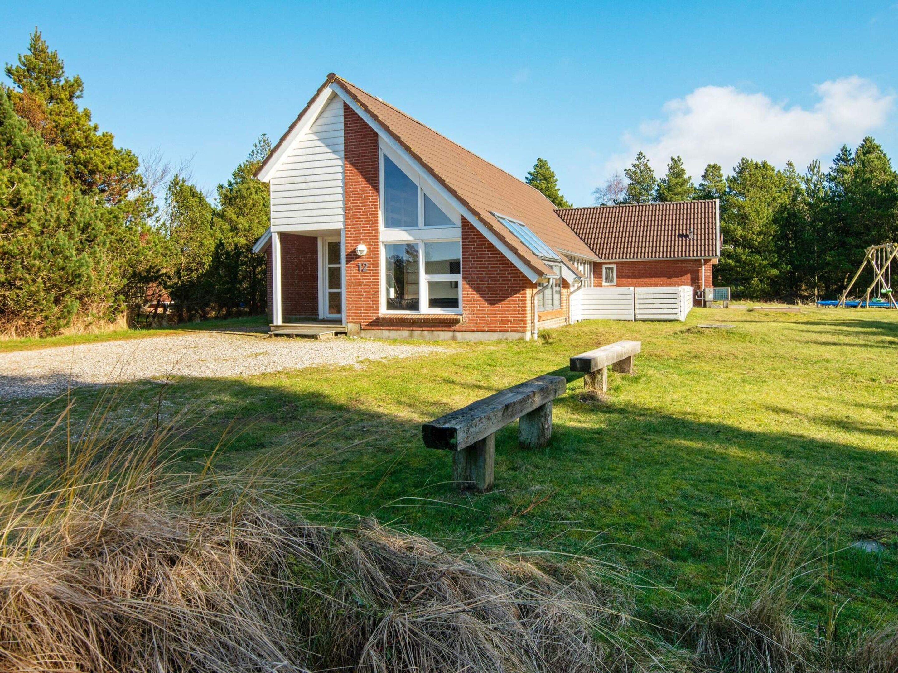 A two-story house with a sloped roof, a visible garage, and a grassy yard with a bench.